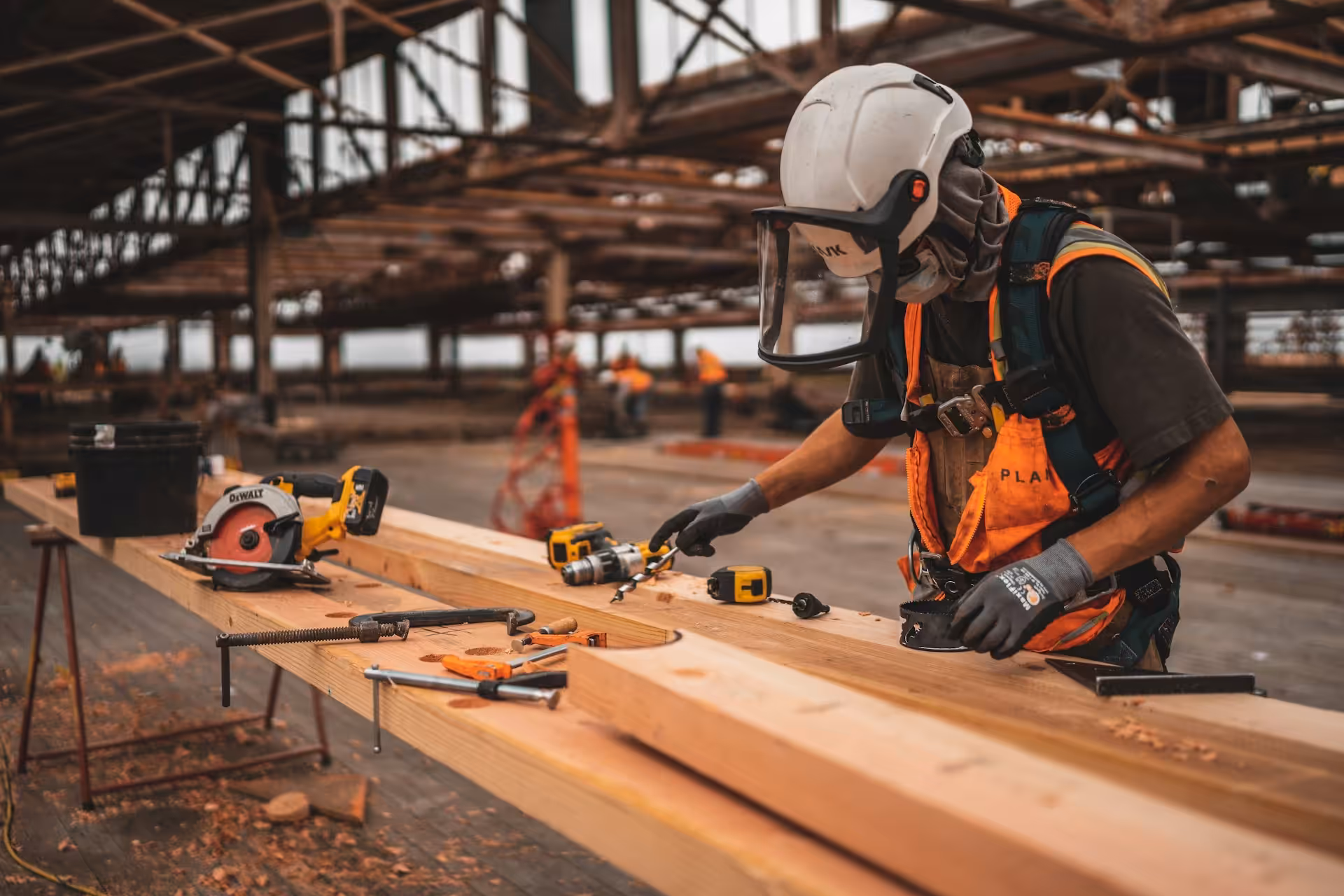 Man in orange and black vest wearing white helmet holding yellow and black power tool